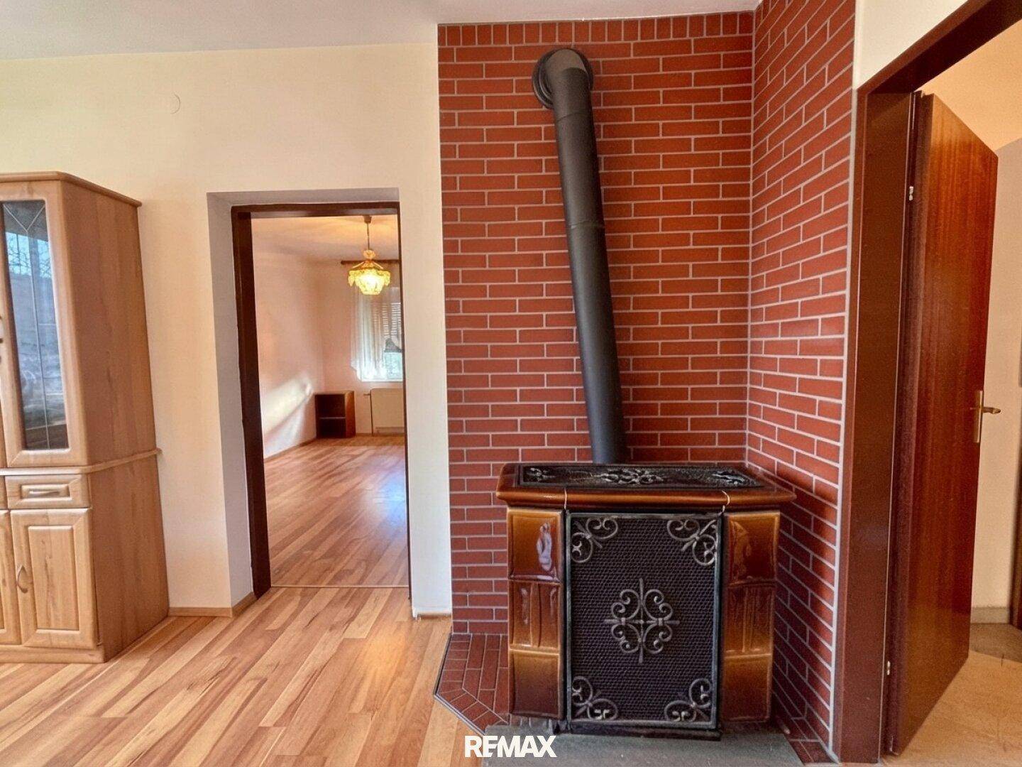 Wohnbereich mit traditionellem Kachelofen, Ziegelwand und Holzboden.