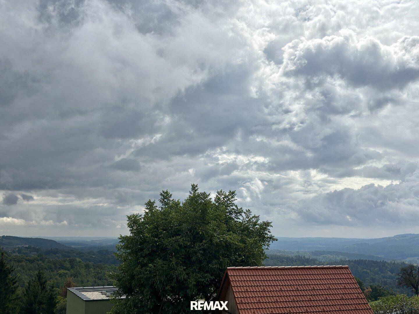 Weitläufiger Blick über die grüne Landschaft und bewaldete Hügel unter dramatischem Himmel.