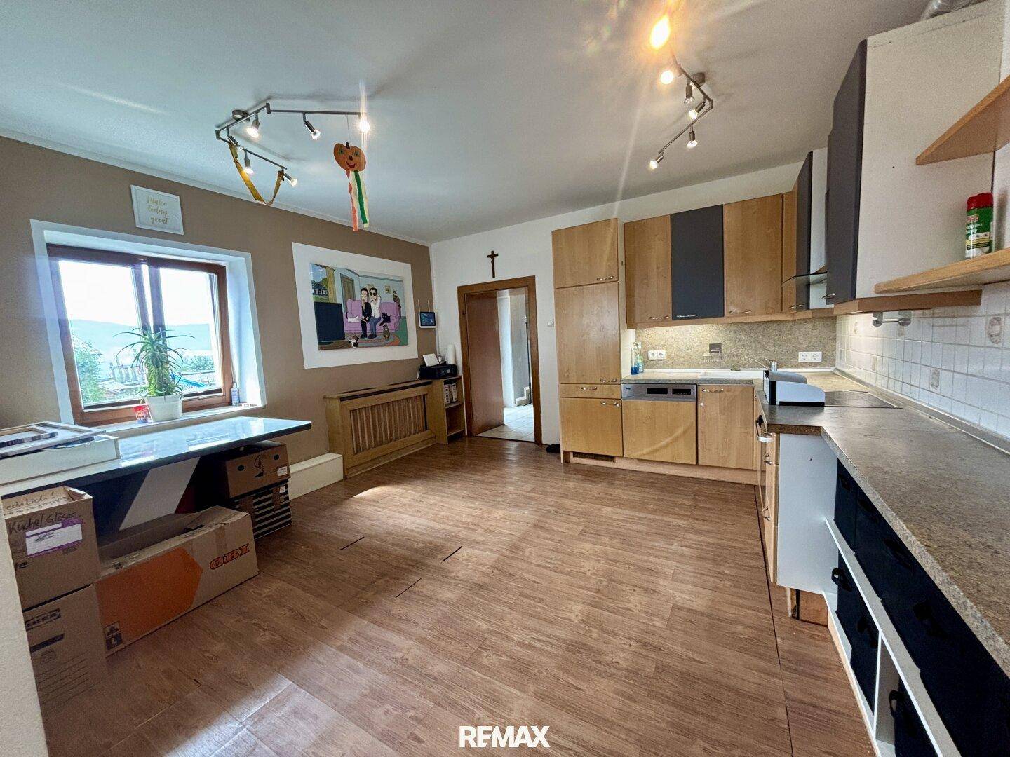 Geräumige Küche mit Holzschränken, Laminatboden und Blick auf die grüne Umgebung.