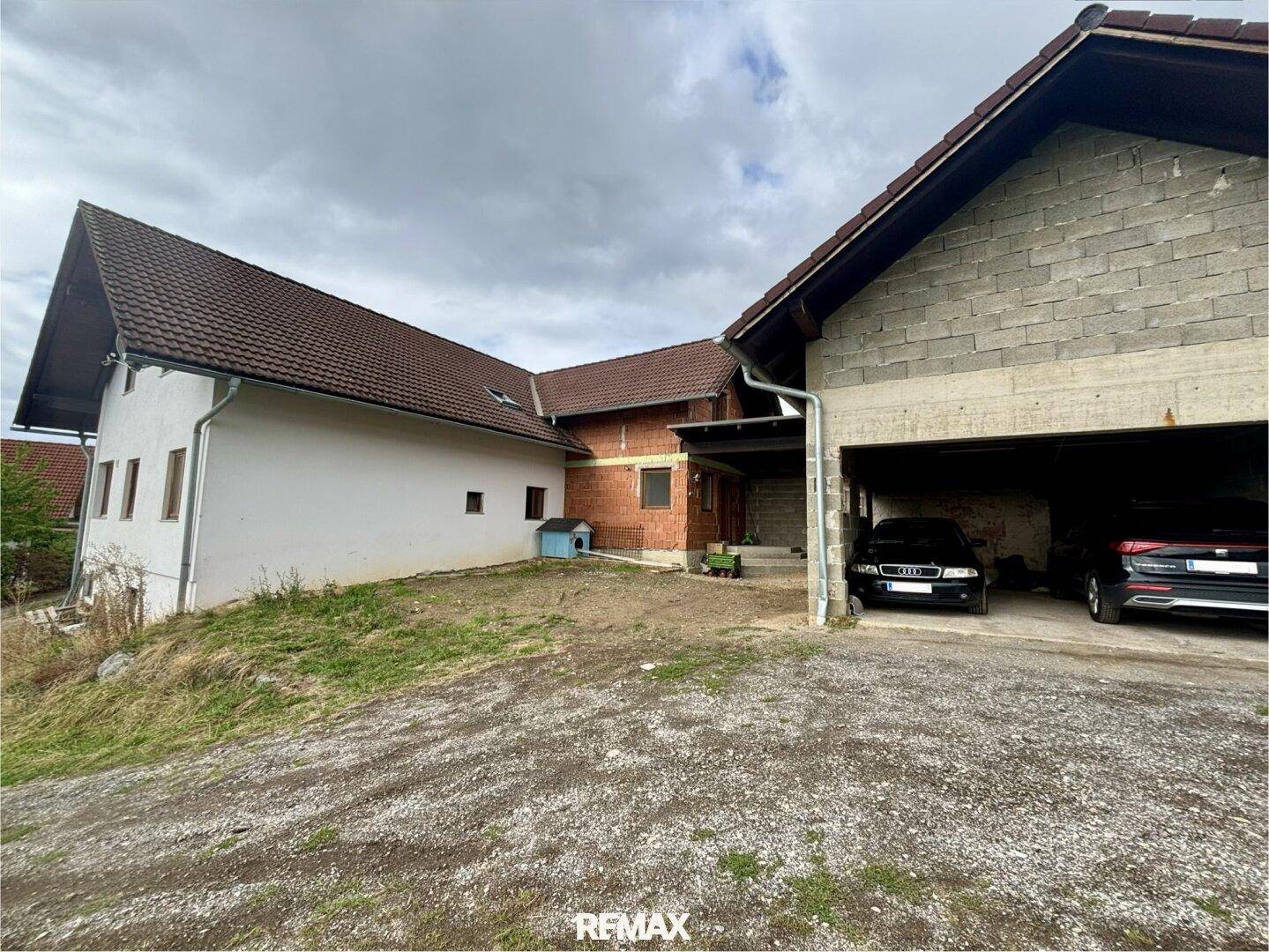 Ländliches Anwesen mit Wohnhaus und separatem Garagengebäude unter bewölktem Himmel.
