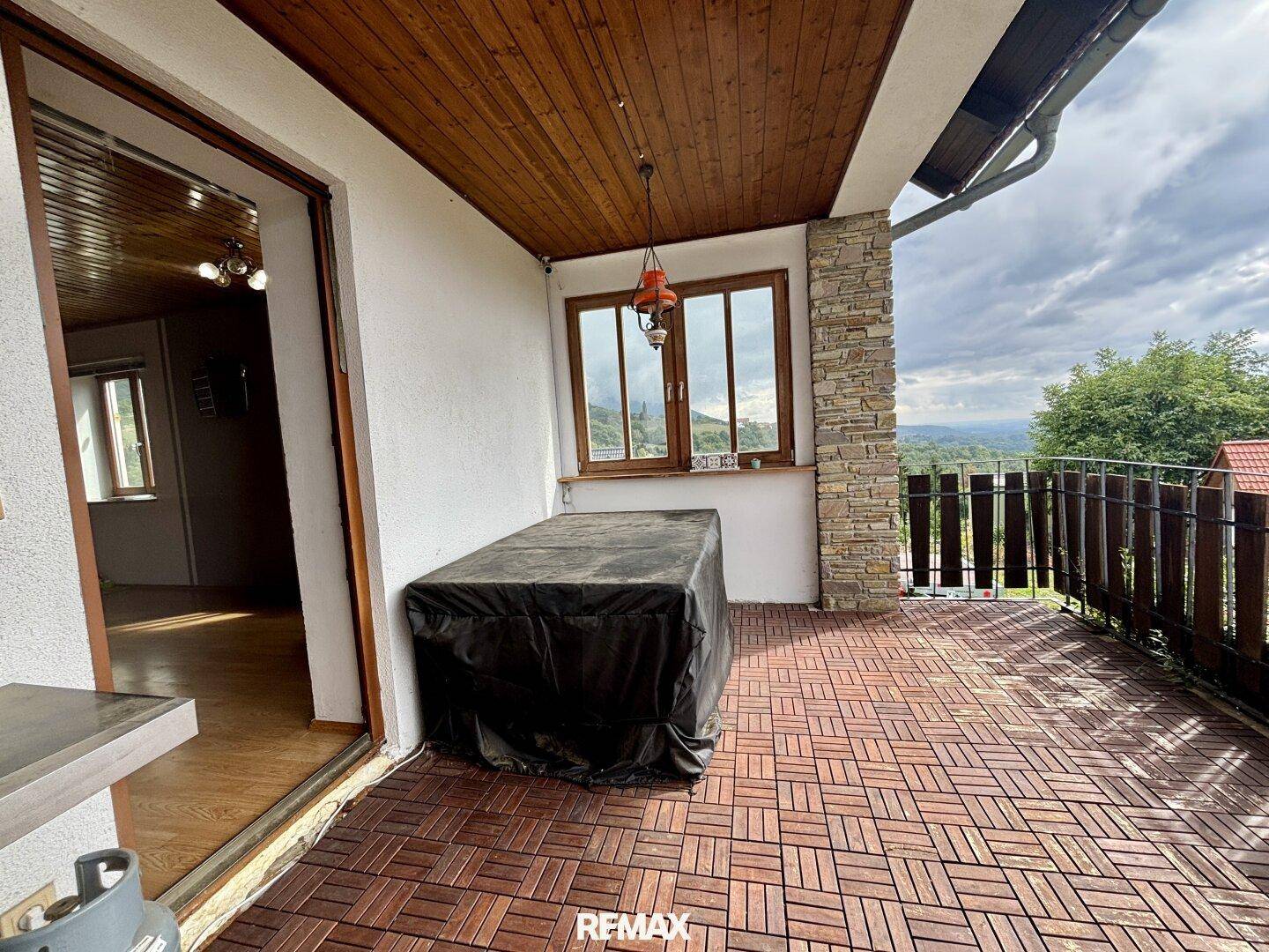 Überdachter Balkon mit Holzboden und weitem Blick über die hügelige Landschaft.