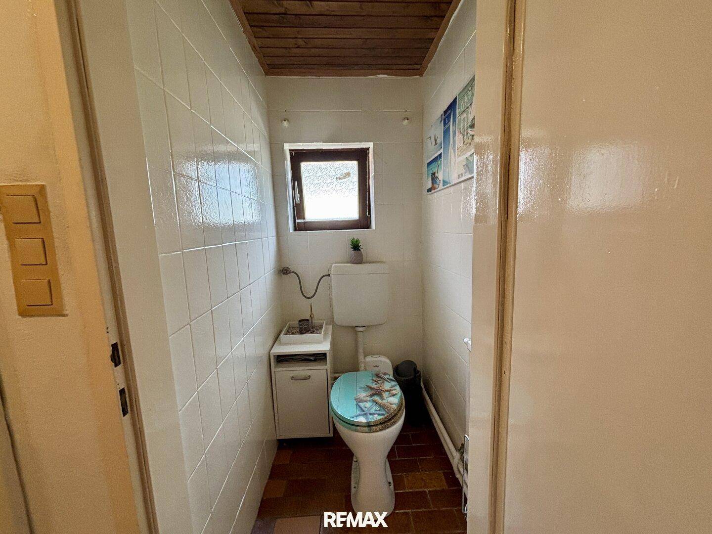 Separate Toilette mit Fliesenboden, Fenster und einfacher Ausstattung.