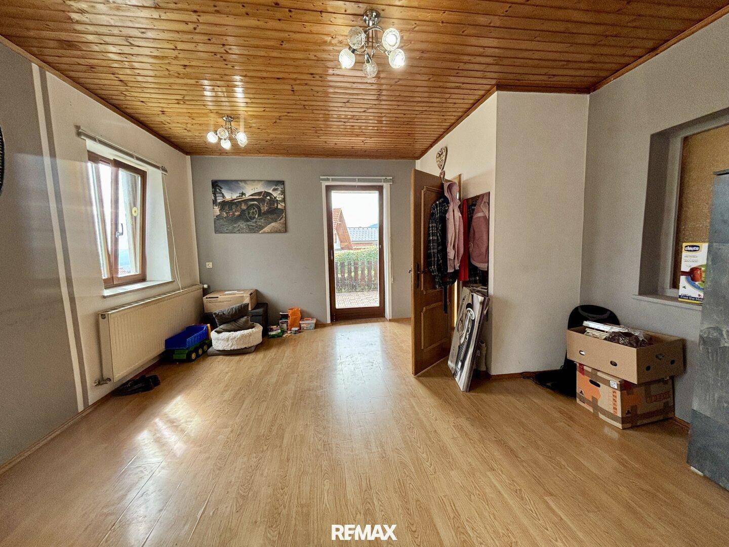 Wohnbereich mit Holzbalkendecke, Laminatboden und Zugang zu einem Außenbereich.