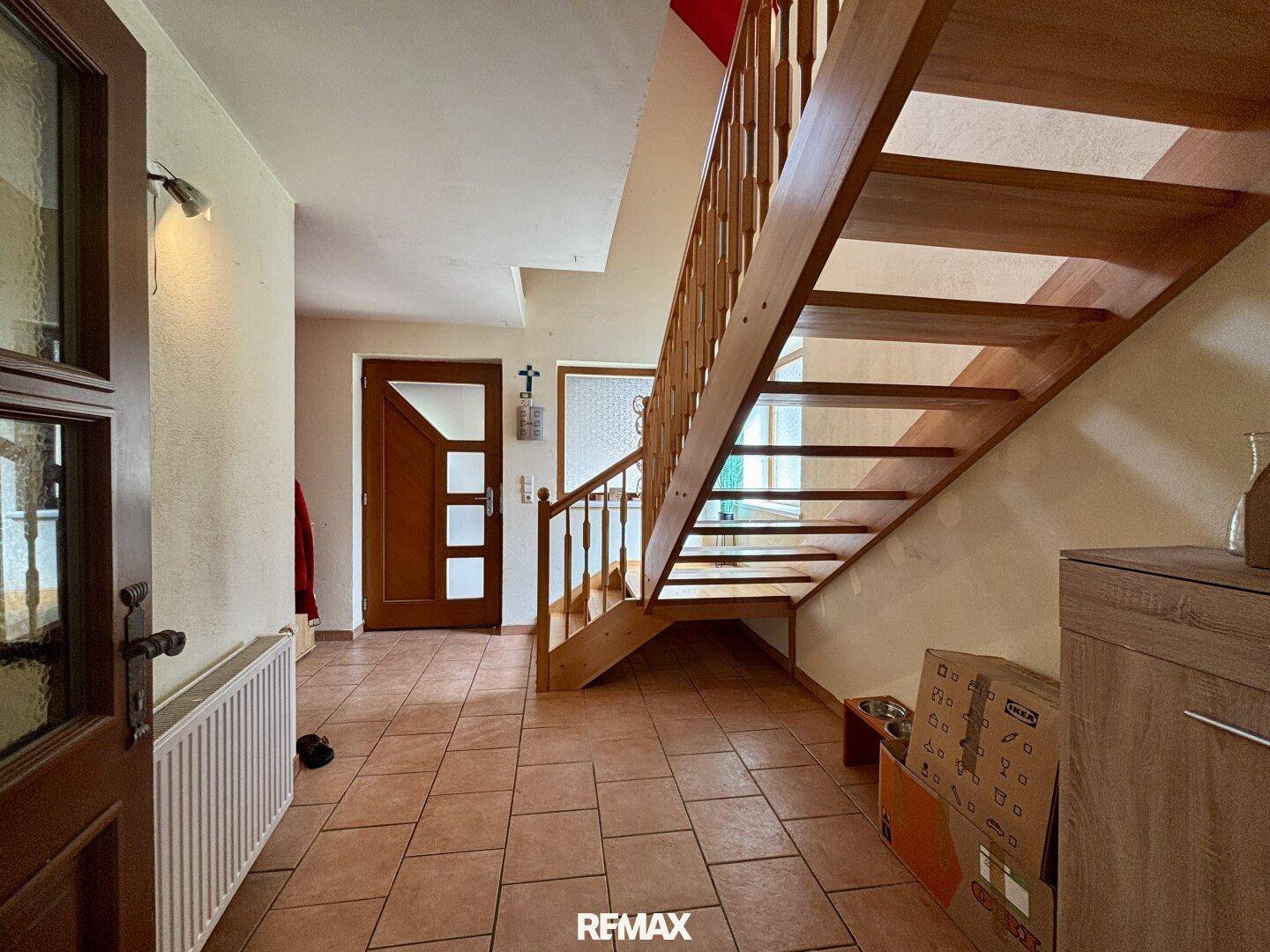 Geräumiger Flur mit Holztreppe, Fliesenboden und Zugang zum Obergeschoss.
