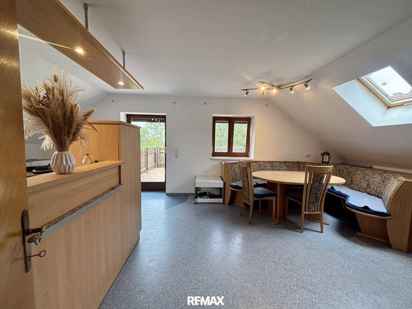 Offener Wohn-Essbereich im Dachgeschoss mit gemütlicher Sitzecke und Zugang zum Balkon.