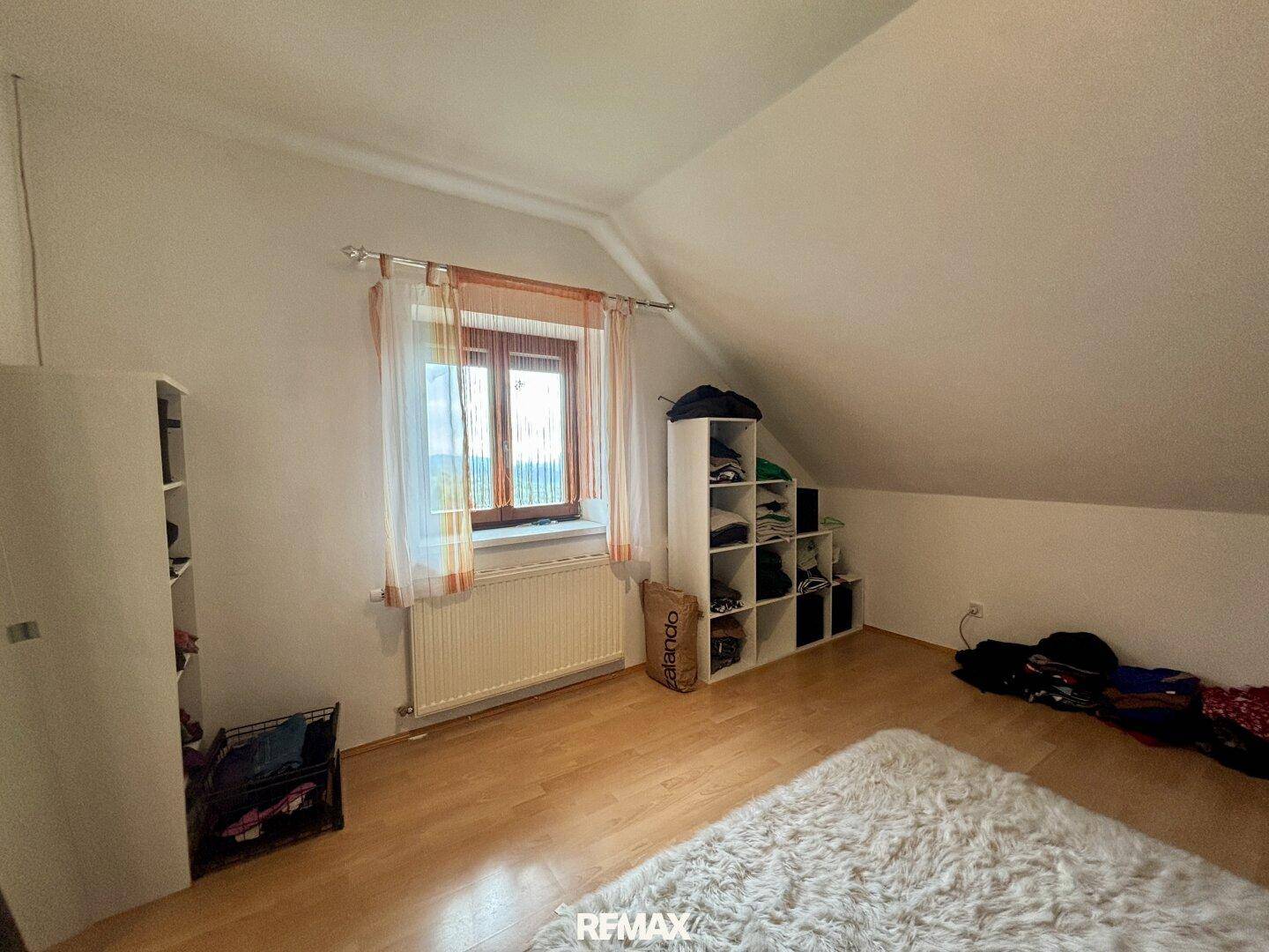 Geräumiges Schlafzimmer im Dachgeschoss mit Laminatboden und Blick ins Grüne.