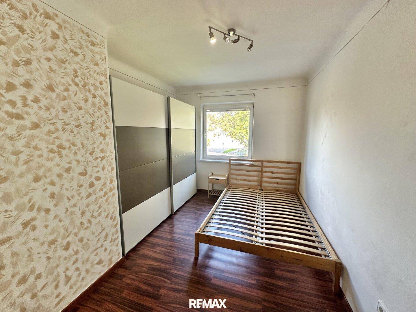 Schlafzimmer mit Holzbettrahmen, großem Schiebeschrank und dekorativer Tapete.