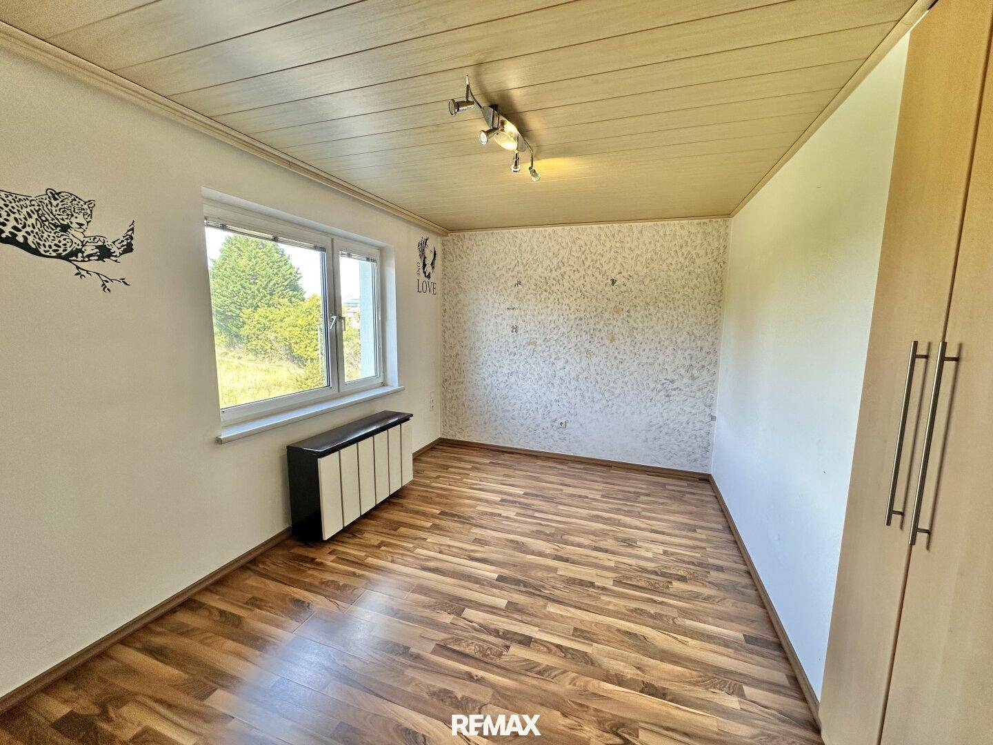 Helles Zimmer mit Holzdecke, Laminatboden und Fenster mit Blick ins Grüne.