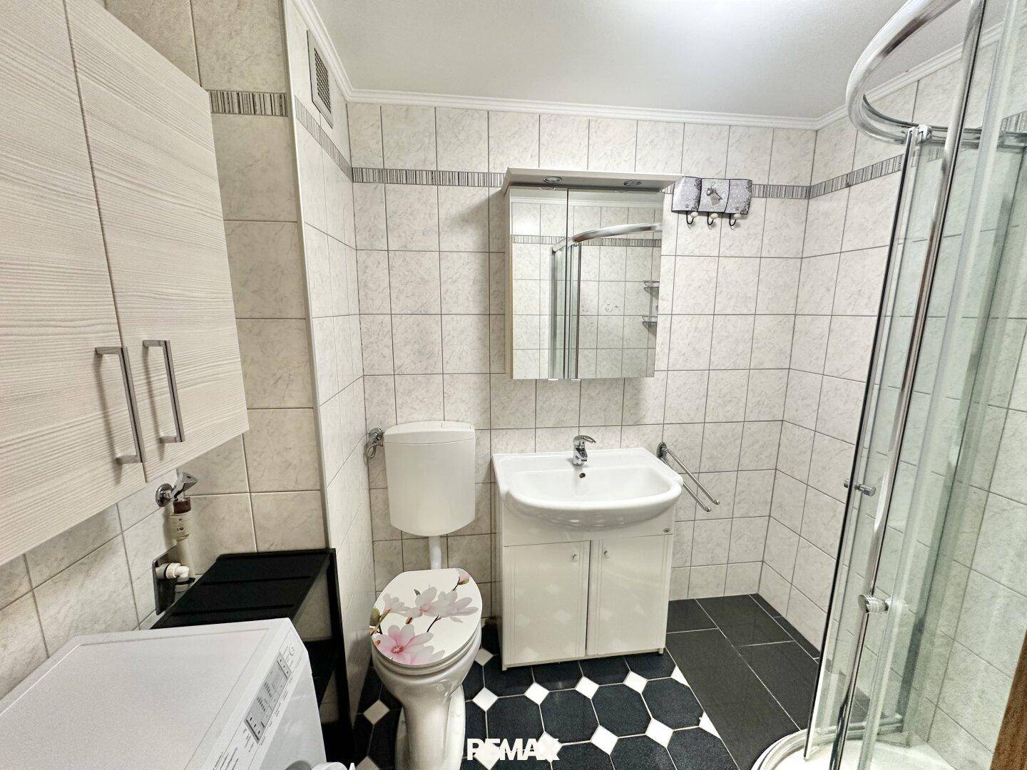 Gefliestes Badezimmer mit Dusche, WC, Waschbecken und Waschmaschine.