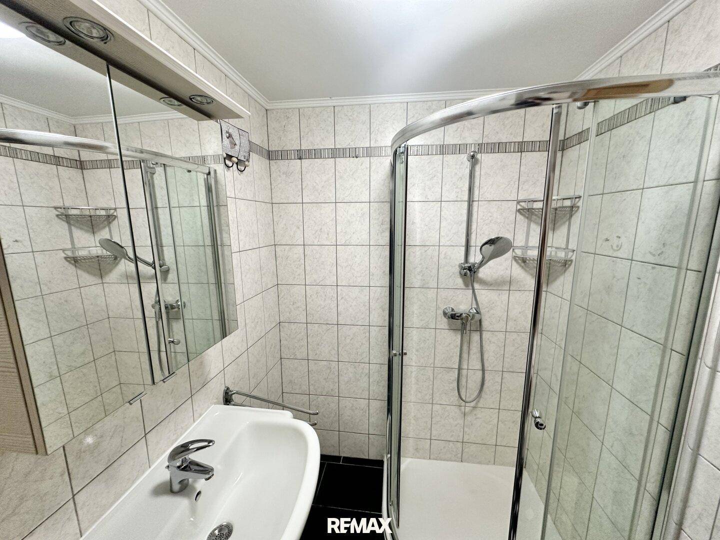 Modern gefliestes Badezimmer mit Duschkabine und Waschbecken.