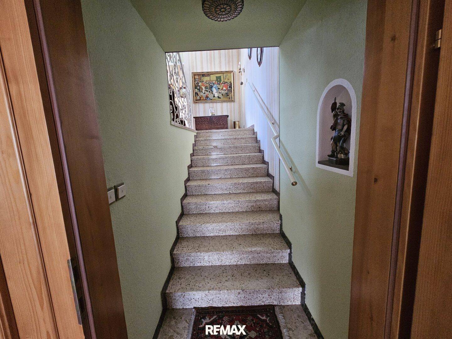 Treppenaufgang mit Terrazzostufen und grün gestrichenen Wänden, der in die obere Etage führt.