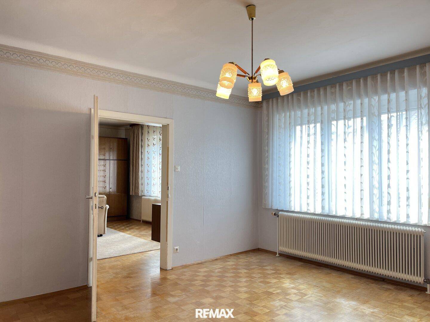 Helles Wohnzimmer mit Parkettboden, blauer Wandgestaltung und Zugang zu einem weiteren Raum.