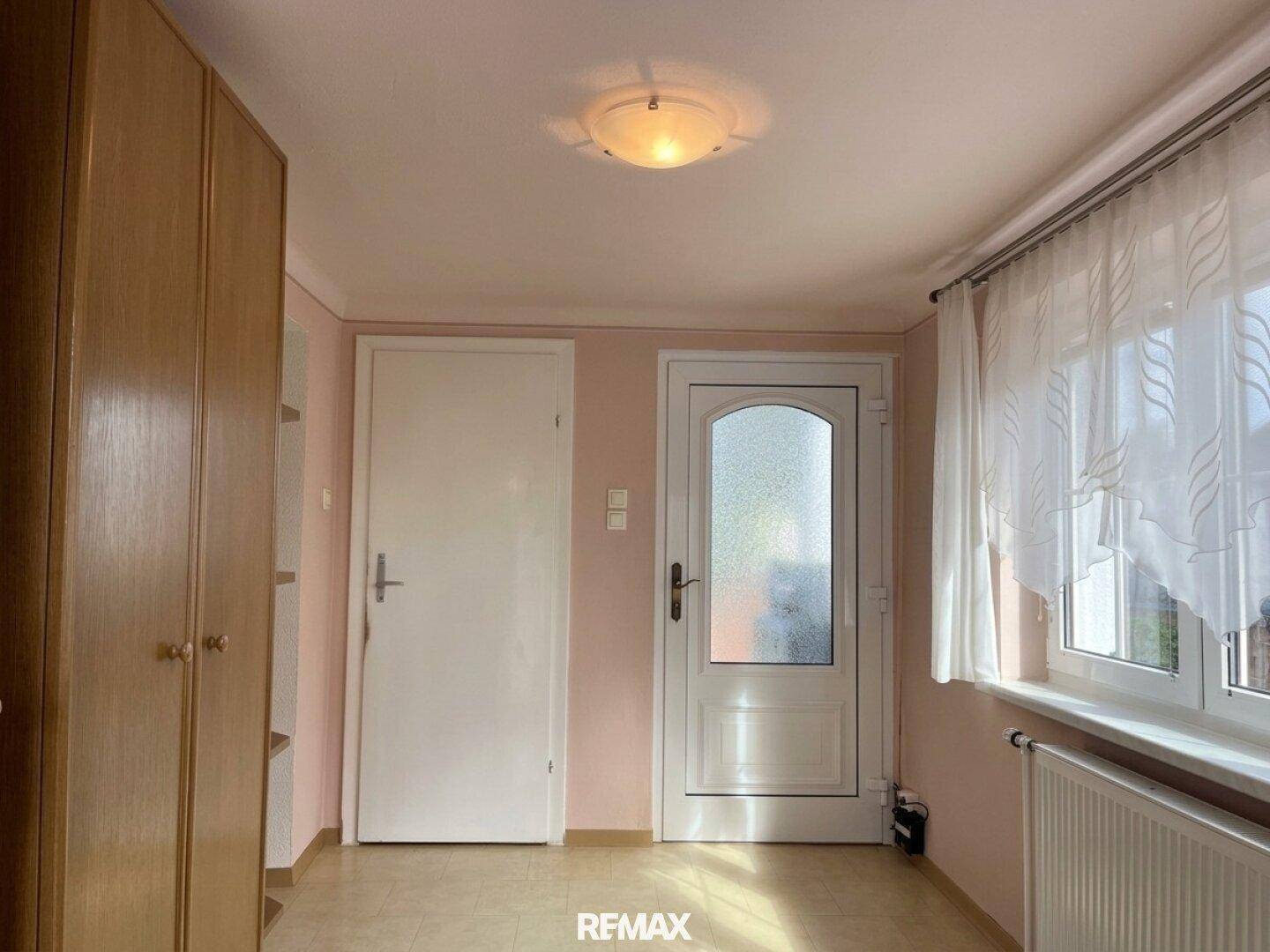 Flur mit zwei weißen Türen, Fenster und einem praktischen Holzschrank für Stauraum.