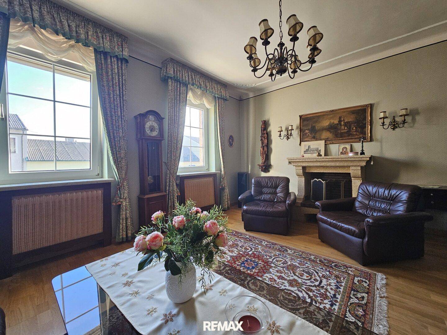 Elegantes Wohnzimmer mit Kamin, Ledersesseln und Holzboden, geschmückt mit einem Kronleuchter.