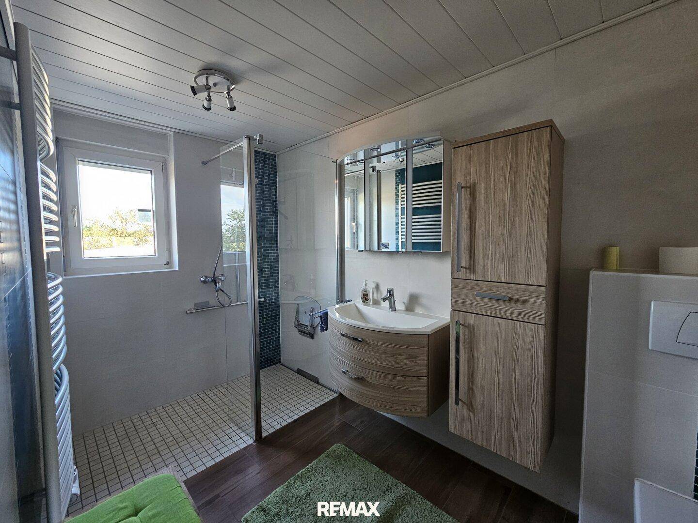 Modernisiertes Badezimmer mit Dusche, Waschbecken und Holzoptik-Bodenfliesen.