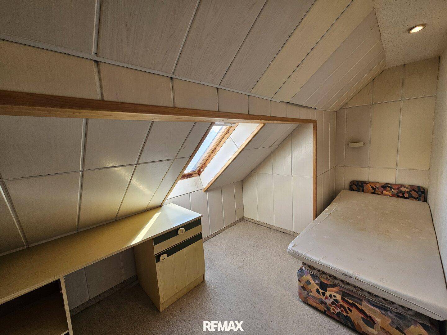 Dachzimmer mit Schreibtisch, Bett und Dachfenster, das natürliches Licht spendet.