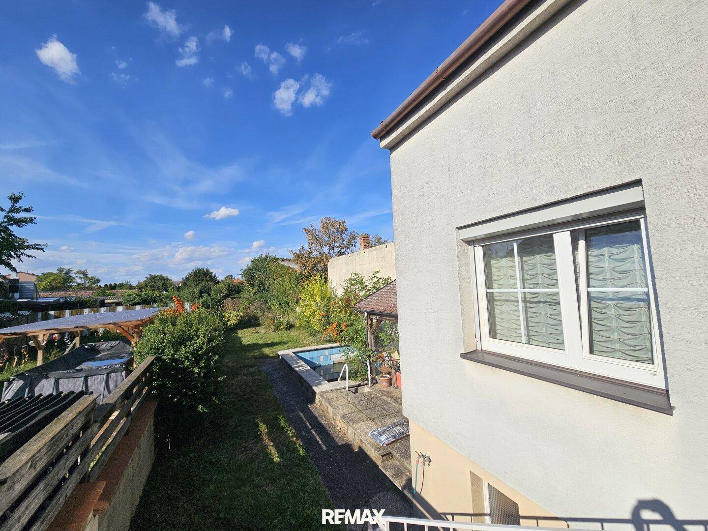 Großer Gartenbereich mit Rasenfläche, kleinem Pool und viel Grün unter blauem Himmel.