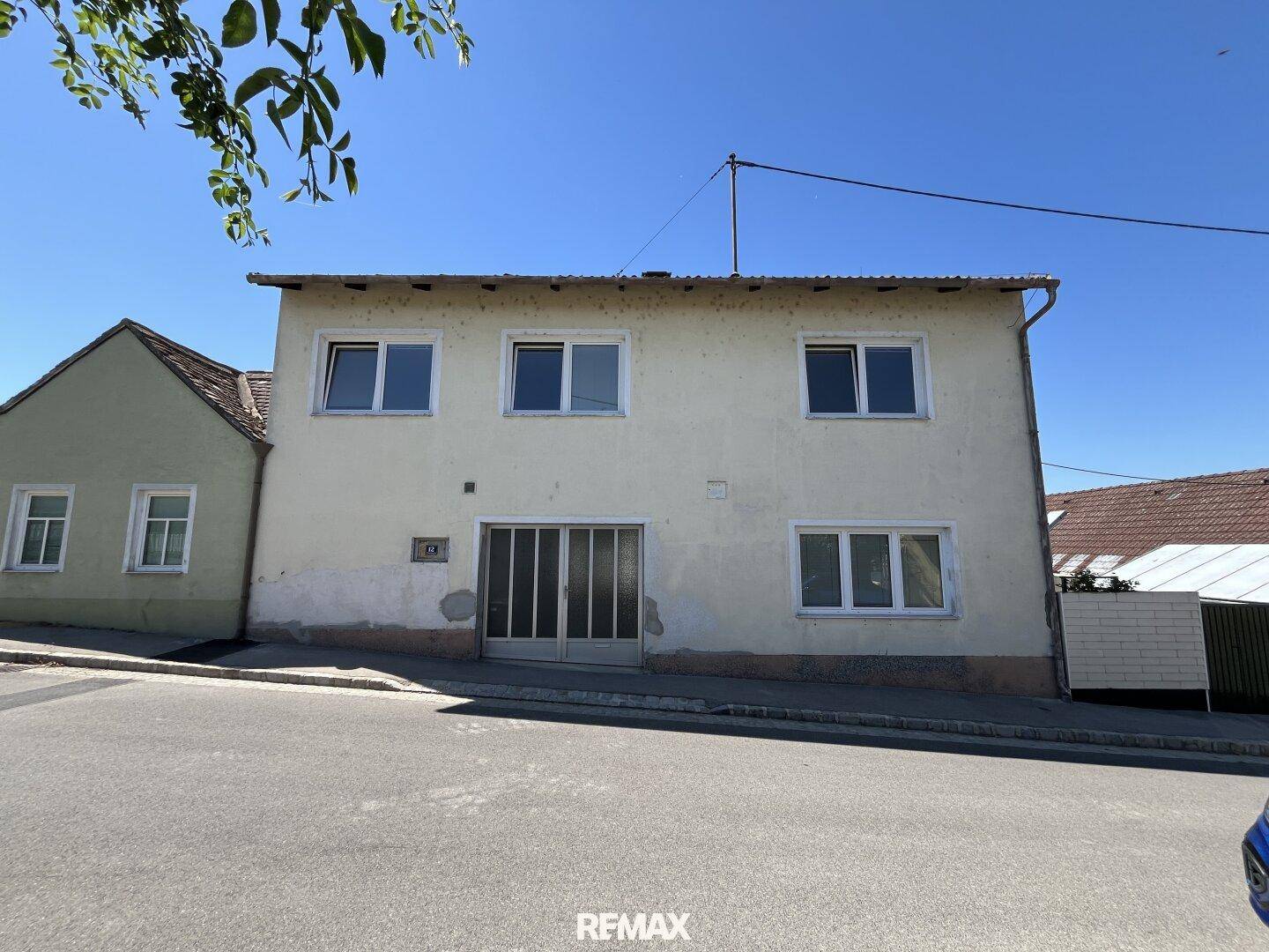 Fassade eines älteren Wohnhauses mit mehreren Fenstern und einer Garagentür an einem sonnigen Tag.