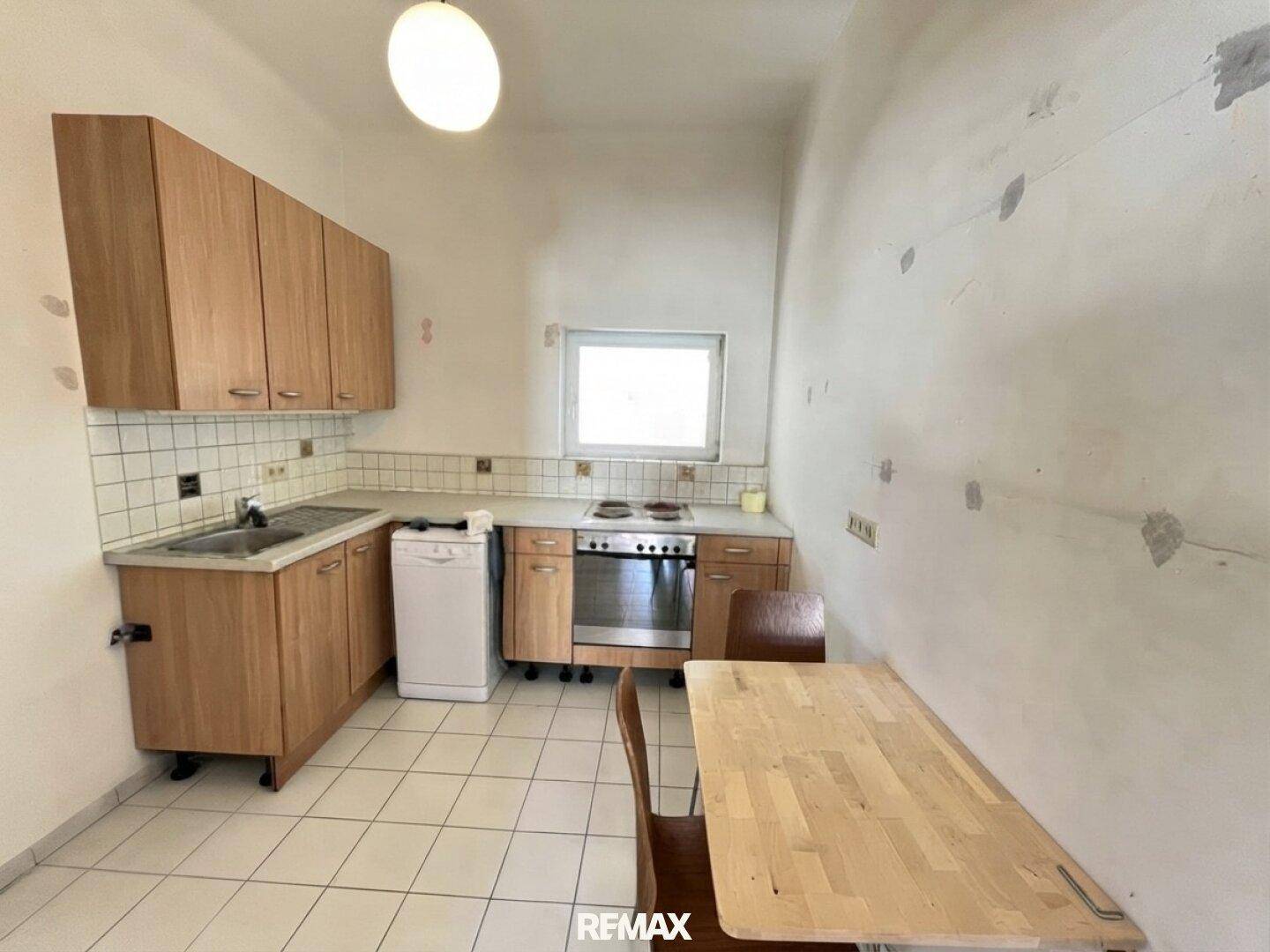 Ältere Küche mit Holzschränken, weißen Fliesen und einem kleinen Esstisch, renovierungsbedürftig.