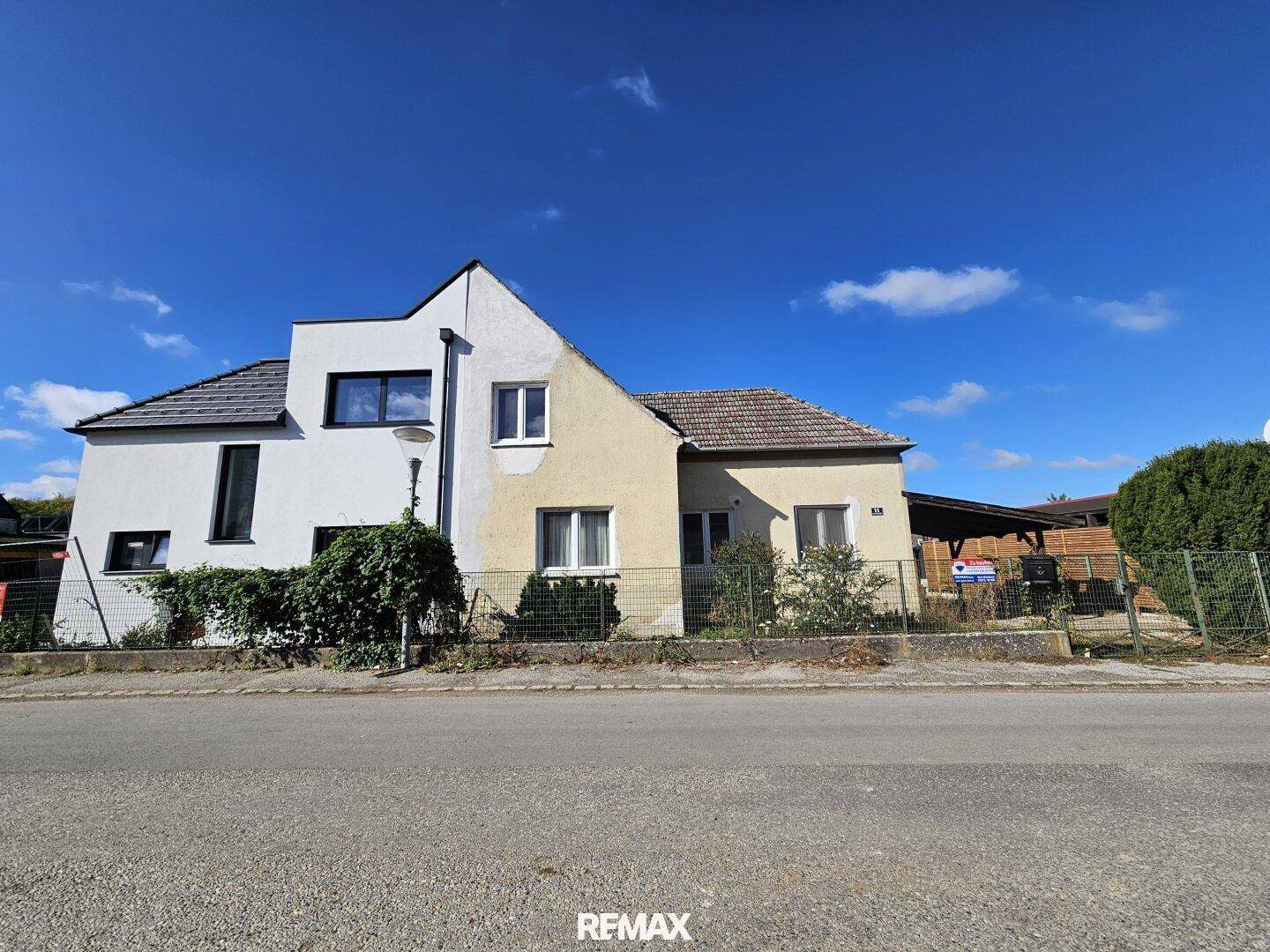 Weitwinkelaufnahme des Hauses mit angrenzendem Carport und Gartenbereich unter strahlend blauem Himmel.