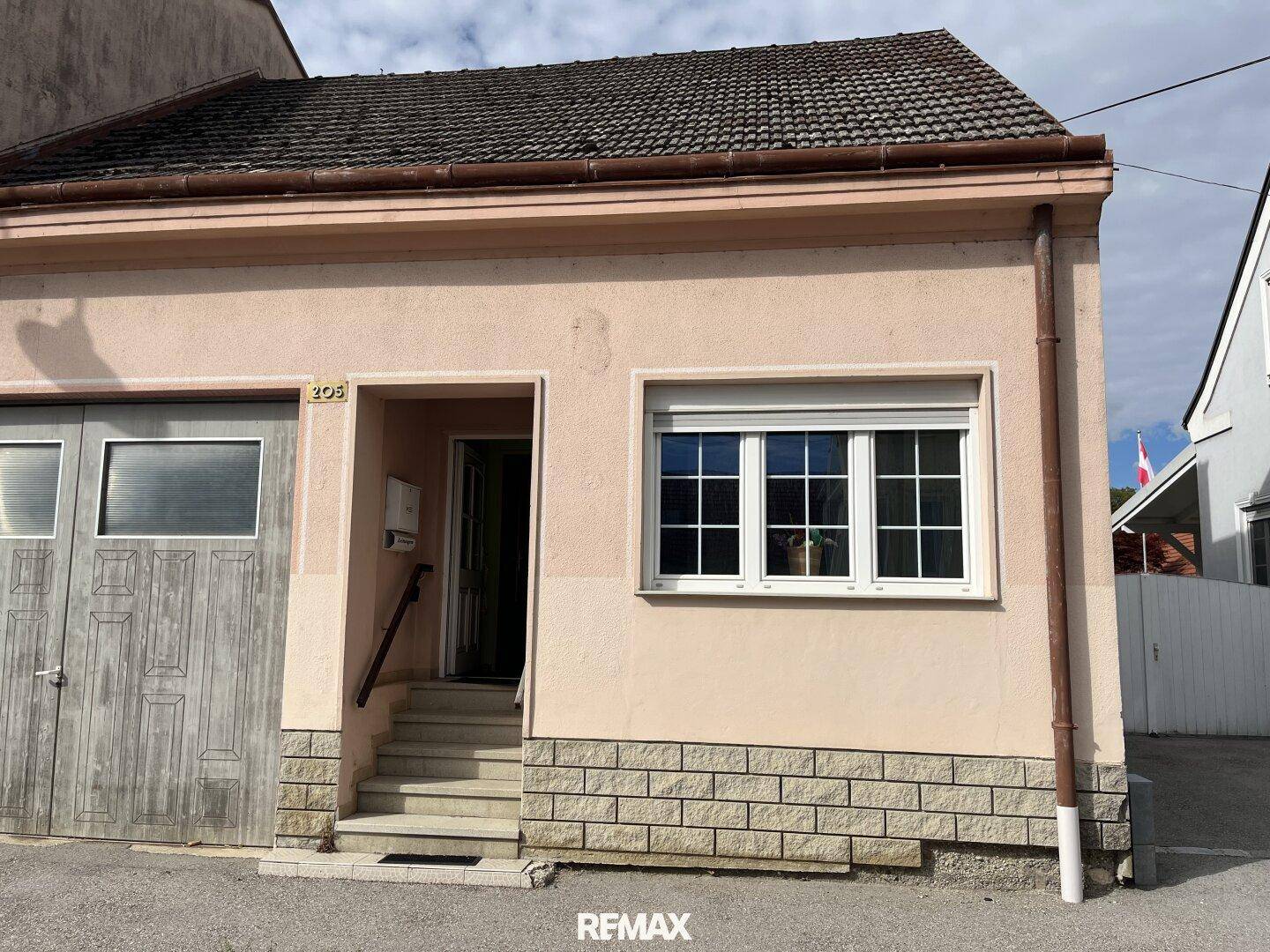 Eingangsbereich eines Hauses mit Steinstufen, Garagentor und Fenster mit Rollladen.