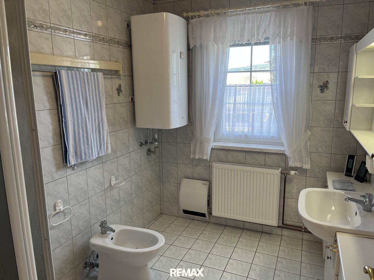 Gefliestes Badezimmer mit Waschbecken, Bidet, Fenster und Heizkörper.