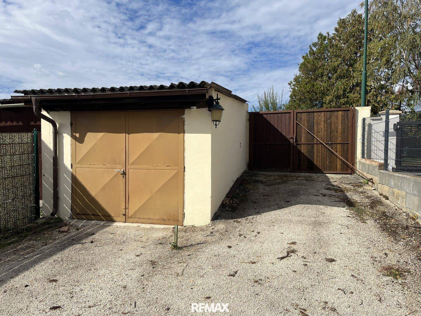 Freistehende Garage mit braunen Toren und Schotterzufahrt, umgeben von einem Holzzaun.