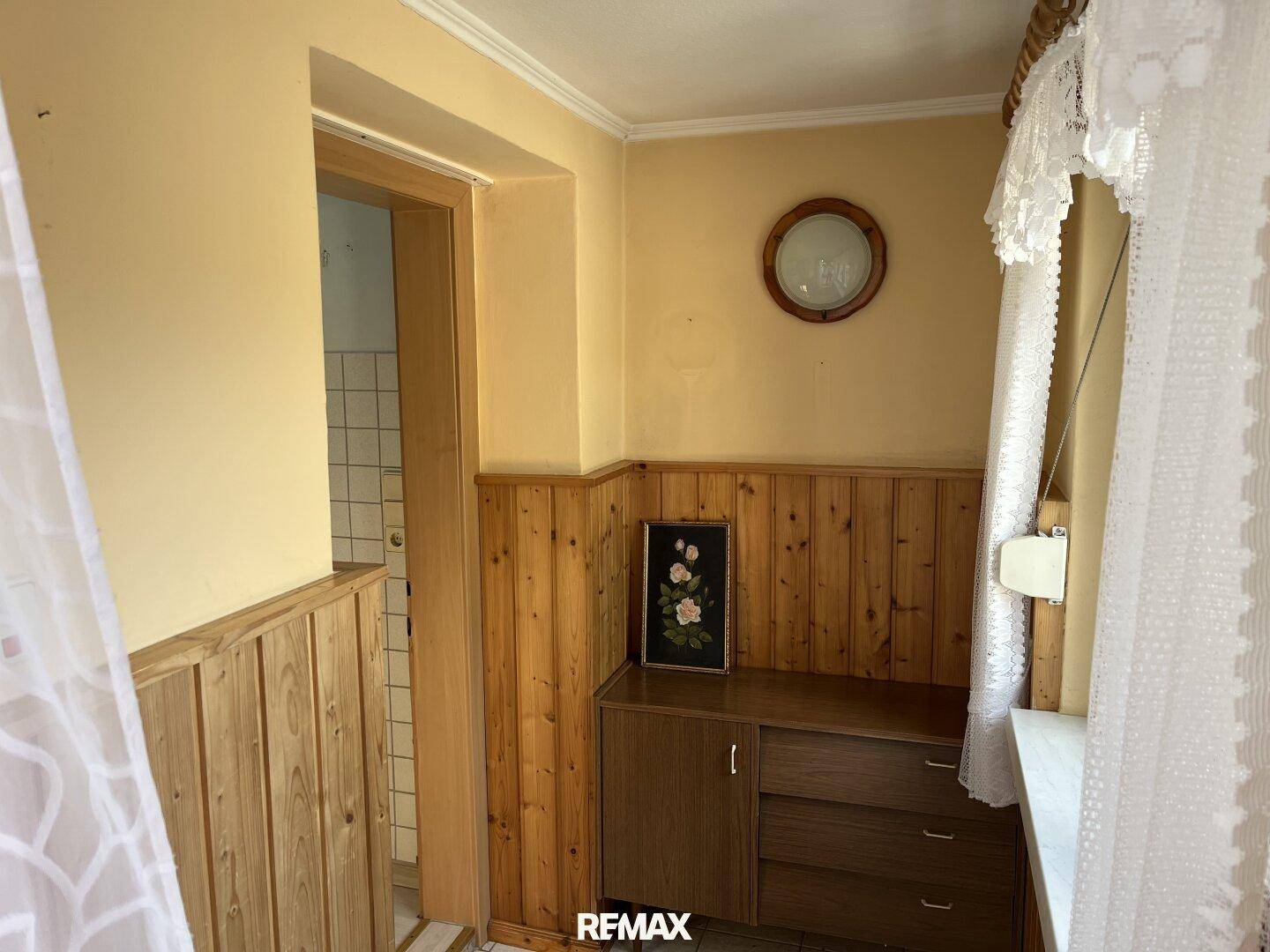 Flur mit Holzvertäfelung, kleinem Schrank und Blick in einen angrenzenden Raum.