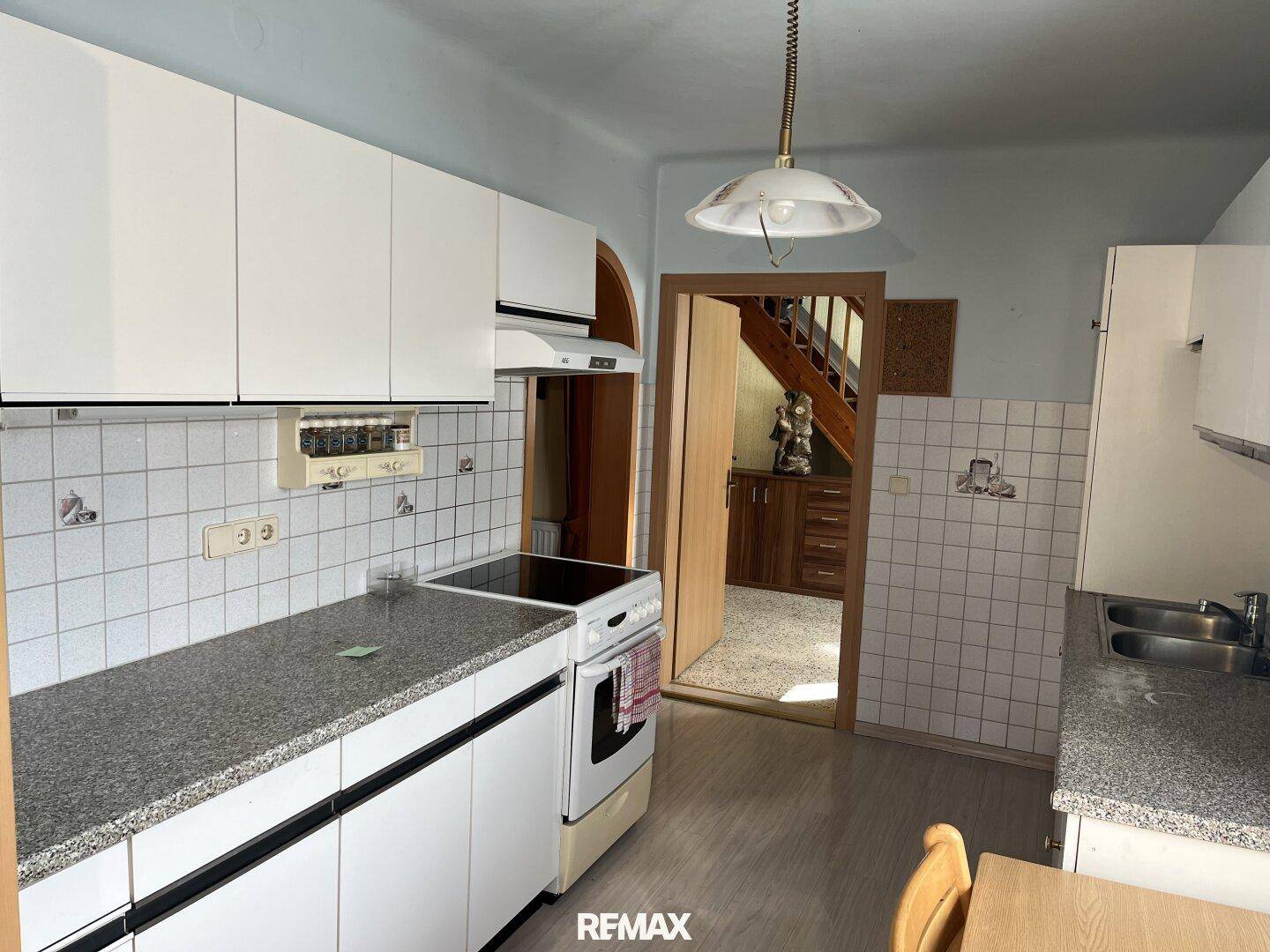 Küche mit weißen Oberschränken, Elektroherd und Blick auf eine Holztreppe im Hintergrund.