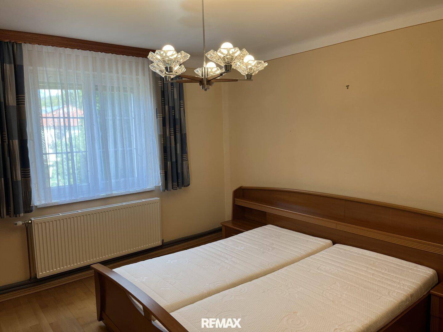 Schlafzimmer mit zwei Einzelbetten, Holzrahmen und Fenster mit Gardinen.