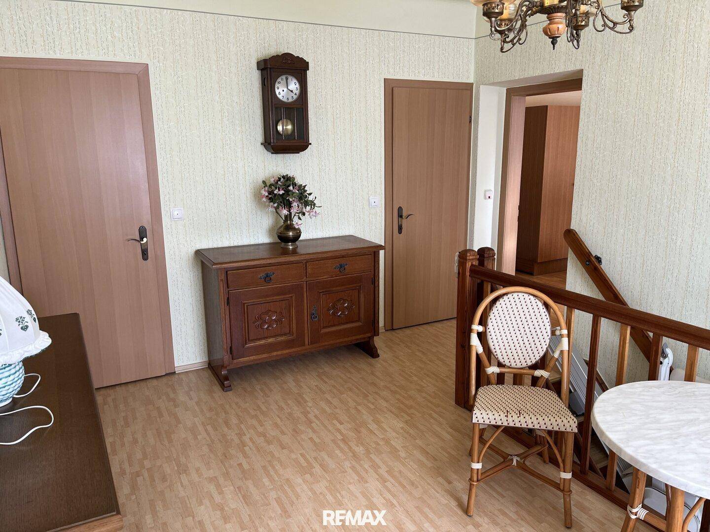 Geräumiger Flur im Obergeschoss mit Kommode, Wanduhr und Zugang zu mehreren Zimmern.