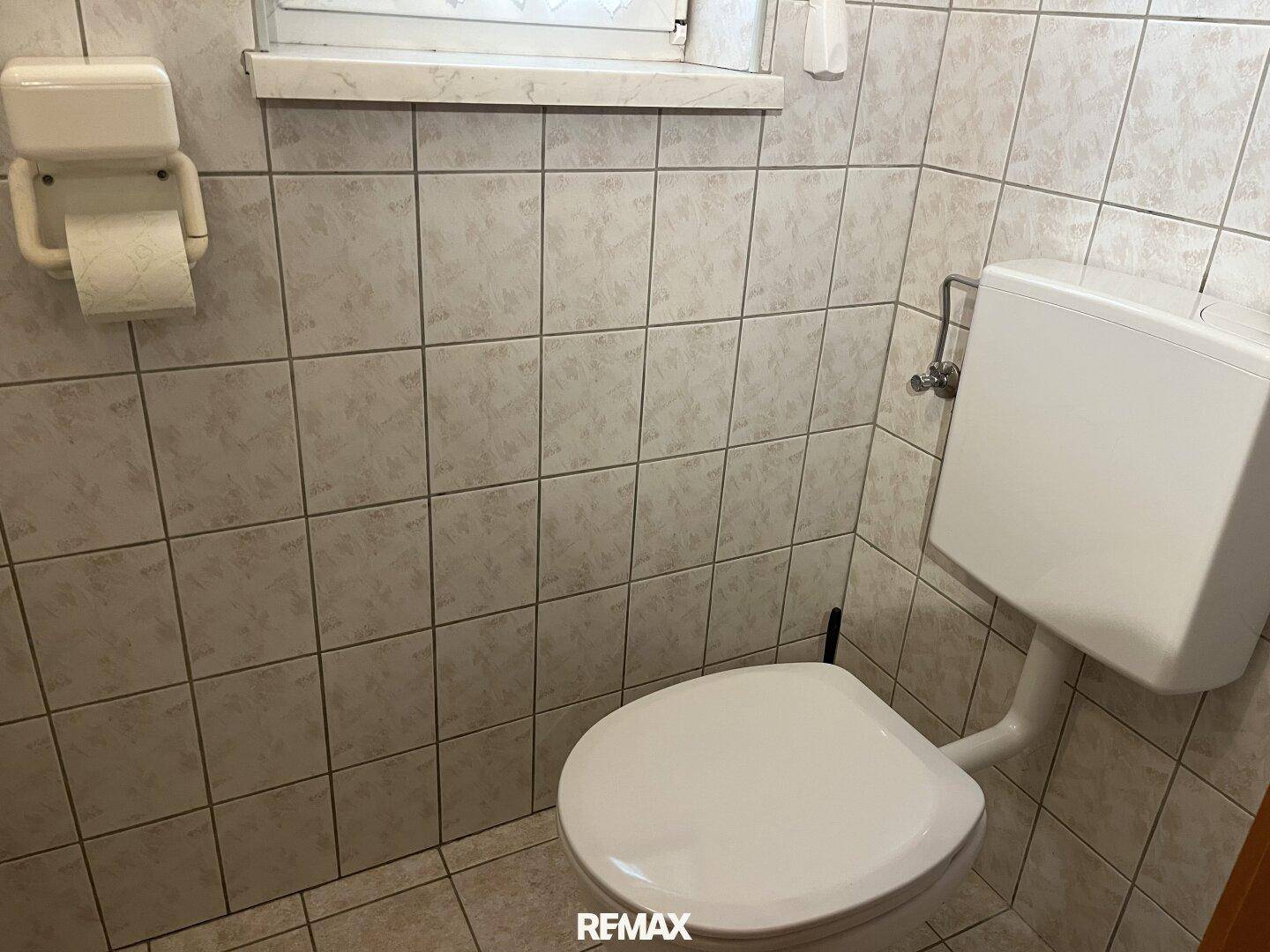 Kleines WC mit hellen Fliesen, Toilette und Fenster für natürliche Belüftung.
