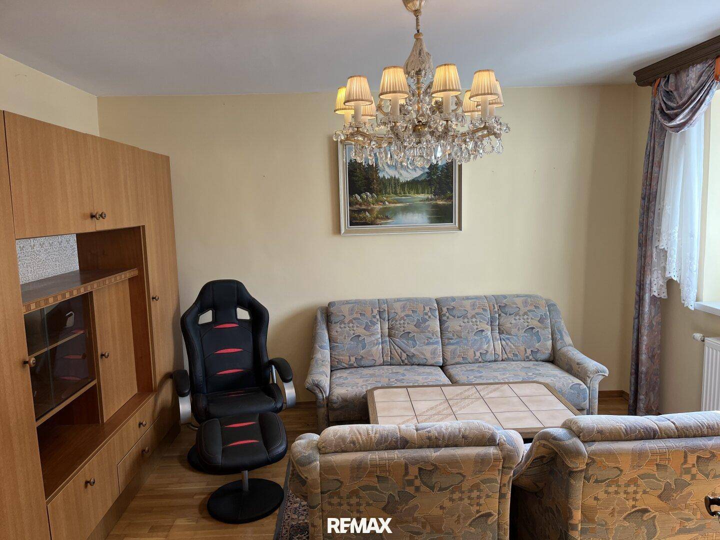 Gemütliches Wohnzimmer mit Sofa, Sessel, Schrankwand und Kronleuchter.