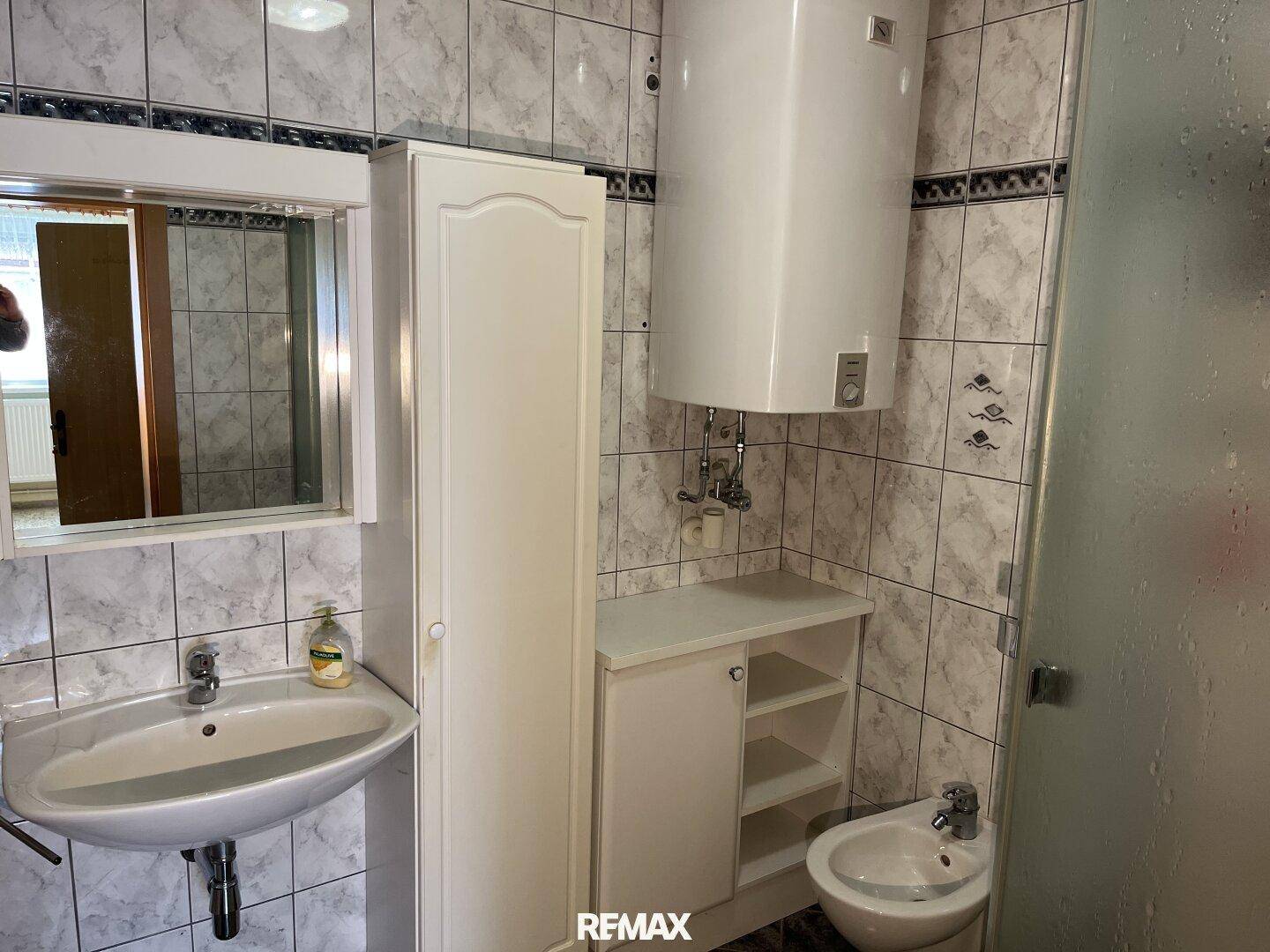 Gefliestes Badezimmer mit Waschbecken, Bidet, Duschkabine und Warmwasserboiler.