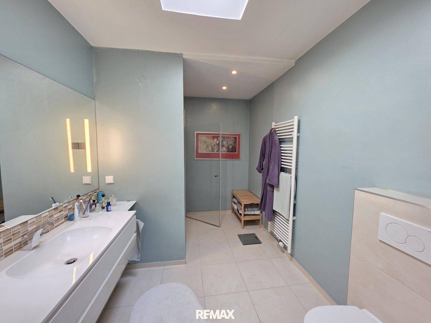 Modernes Badezimmer mit großem Waschtisch, begehbarer Dusche und Oberlicht für natürliches Licht.