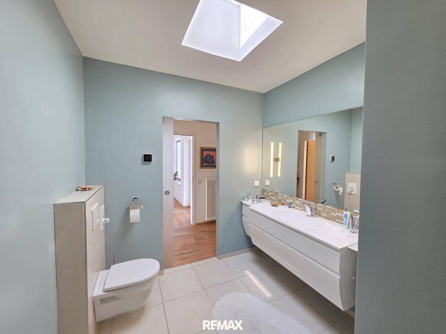 Helles Badezimmer mit modernem Design, großem Spiegel, Waschtisch und Schiebetür zum Flur.