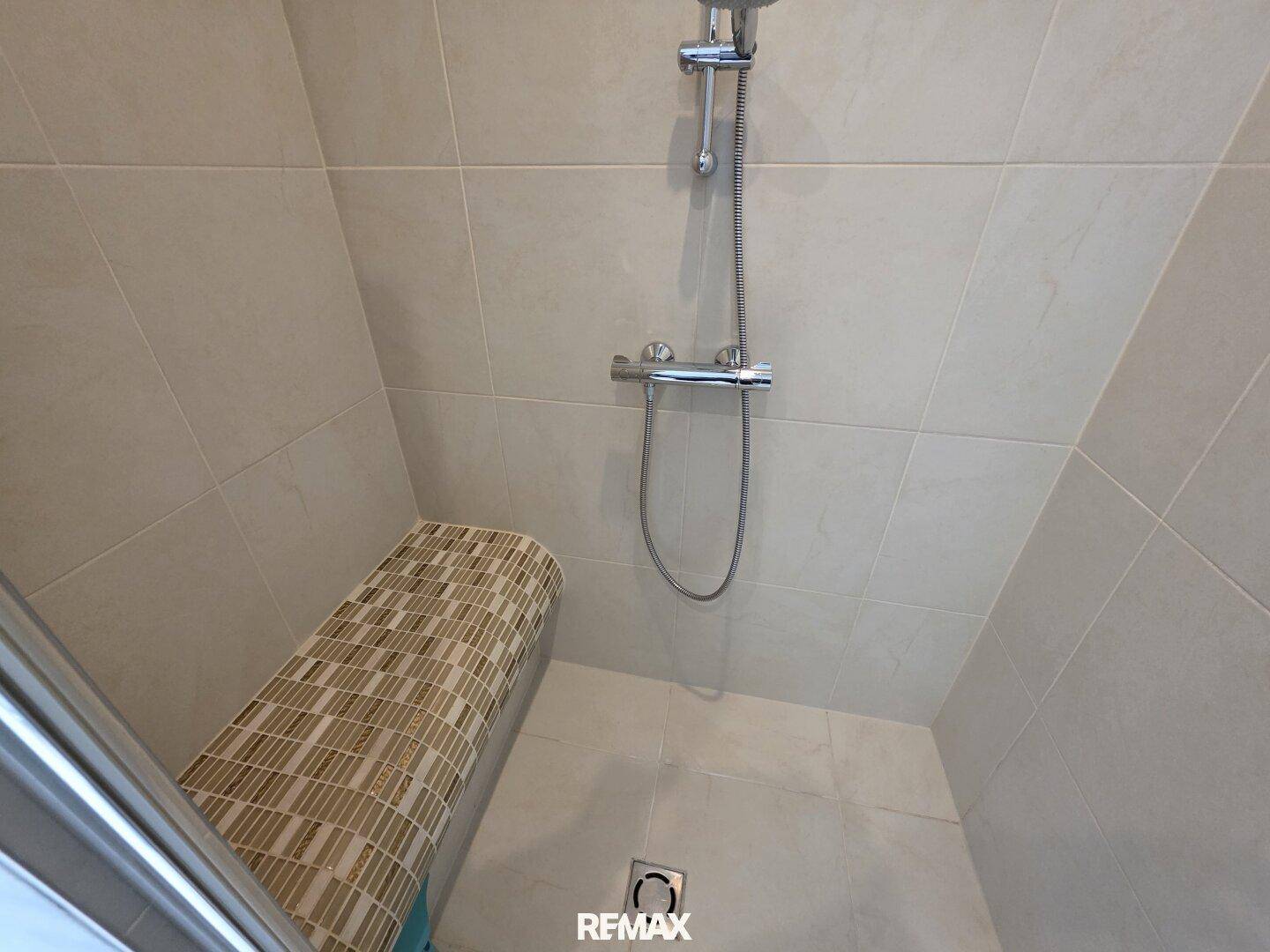 Detaillierte Ansicht einer modernen, gefliesten Dusche mit Sitzbank und Handbrause.