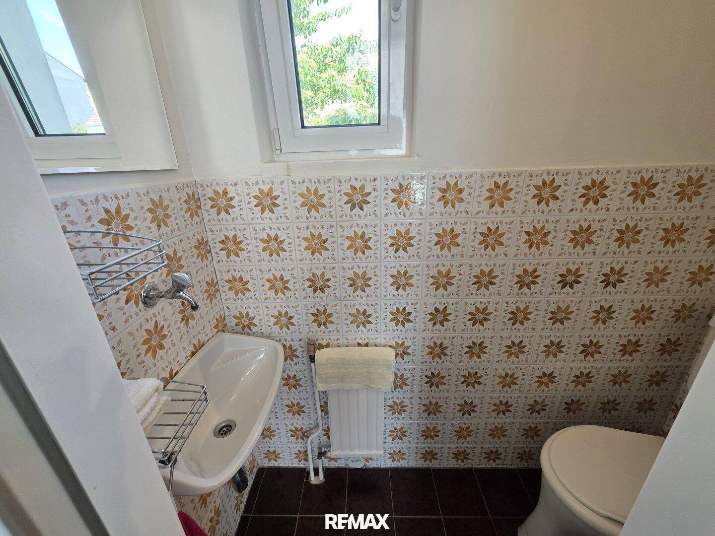 Kleines Gäste-WC mit auffälligen Blumenfliesen, Fenster und Handwaschbecken.
