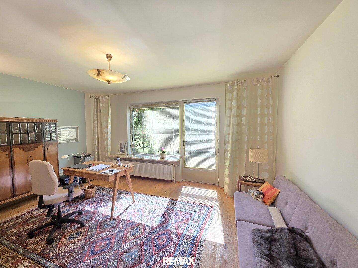 Helles Arbeitszimmer mit Holzfußboden, großem Fenster und einem gemütlichen Sofa.
