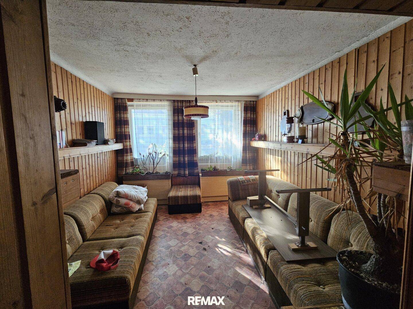 Rustikales Wohnzimmer mit Holzvertäfelung, gemustertem Teppich und älteren Sofas.