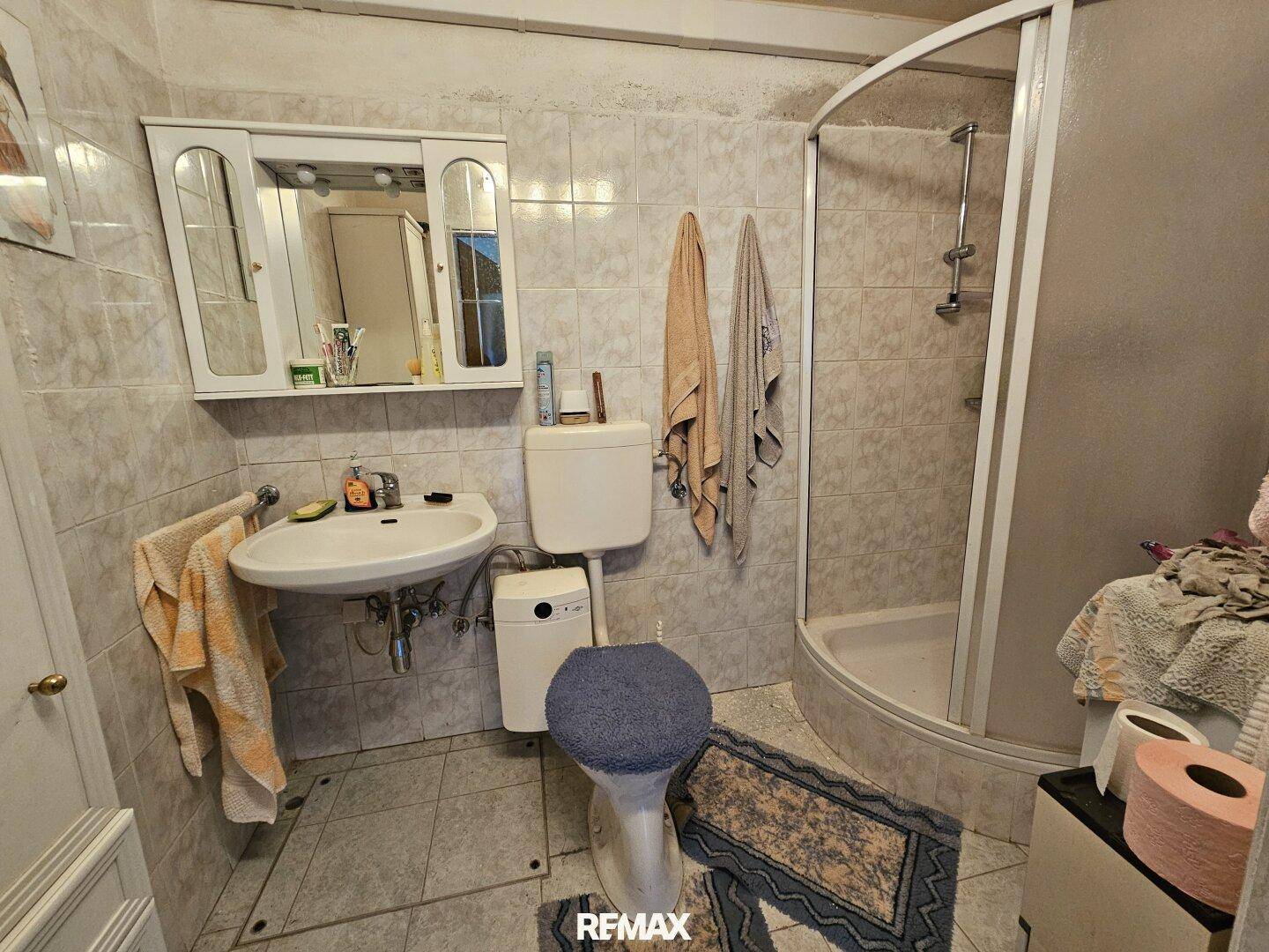 Kleines Badezimmer mit weißen Fliesen, Dusche und einfacher Sanitärausstattung.