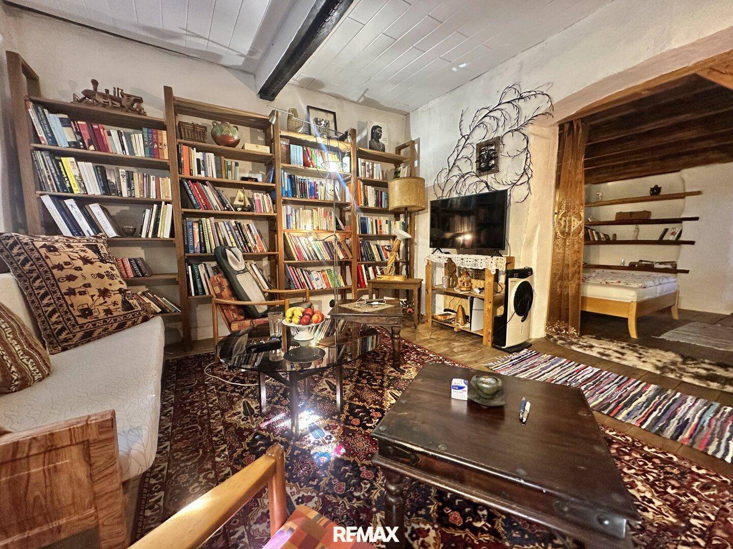Gemütliches Wohnzimmer mit großem Bücherregal, Teppichboden und Blick in ein angrenzendes Schlafzimmer.