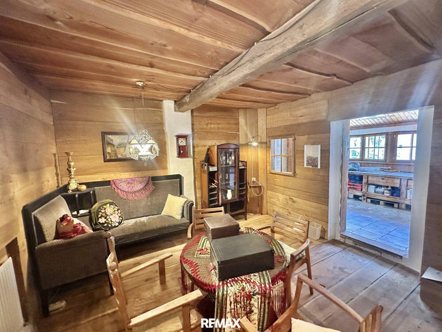 Rustikales Wohnzimmer mit Holzvertäfelung, Holzboden und traditionellen Möbeln, offen zum Flur.