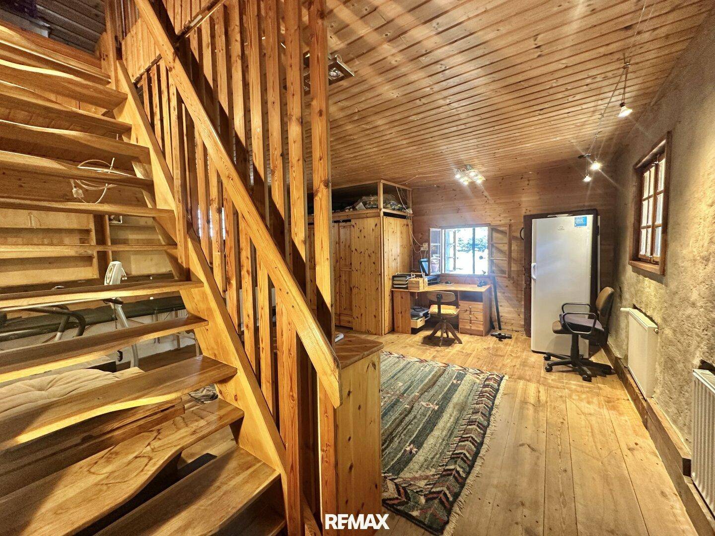 Raum mit Holztreppe, Holzboden und einem Arbeitsbereich mit Schreibtisch und Schrank.
