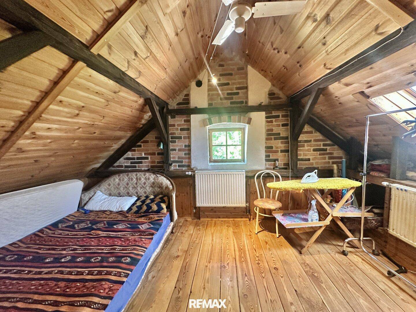Gemütlicher Dachbodenraum mit Holzboden, schrägen Wänden und einem Bett, ideal als Gästezimmer.