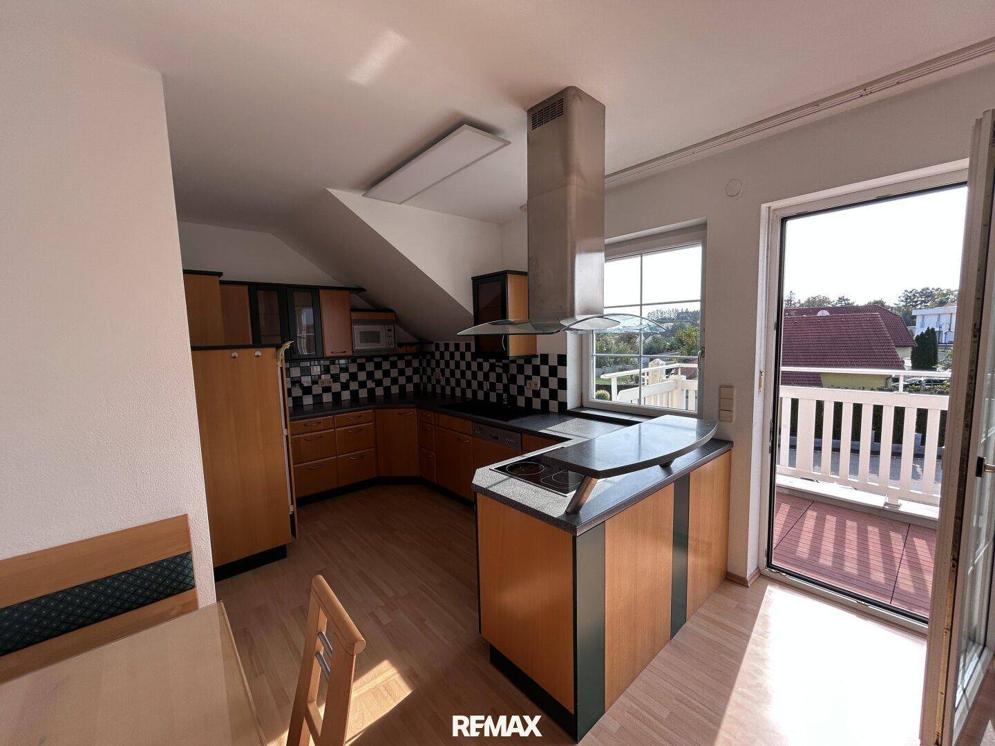 Funktionale Küche mit Holzelementen, Kochinsel und direktem Zugang zu einem sonnigen Balkon.