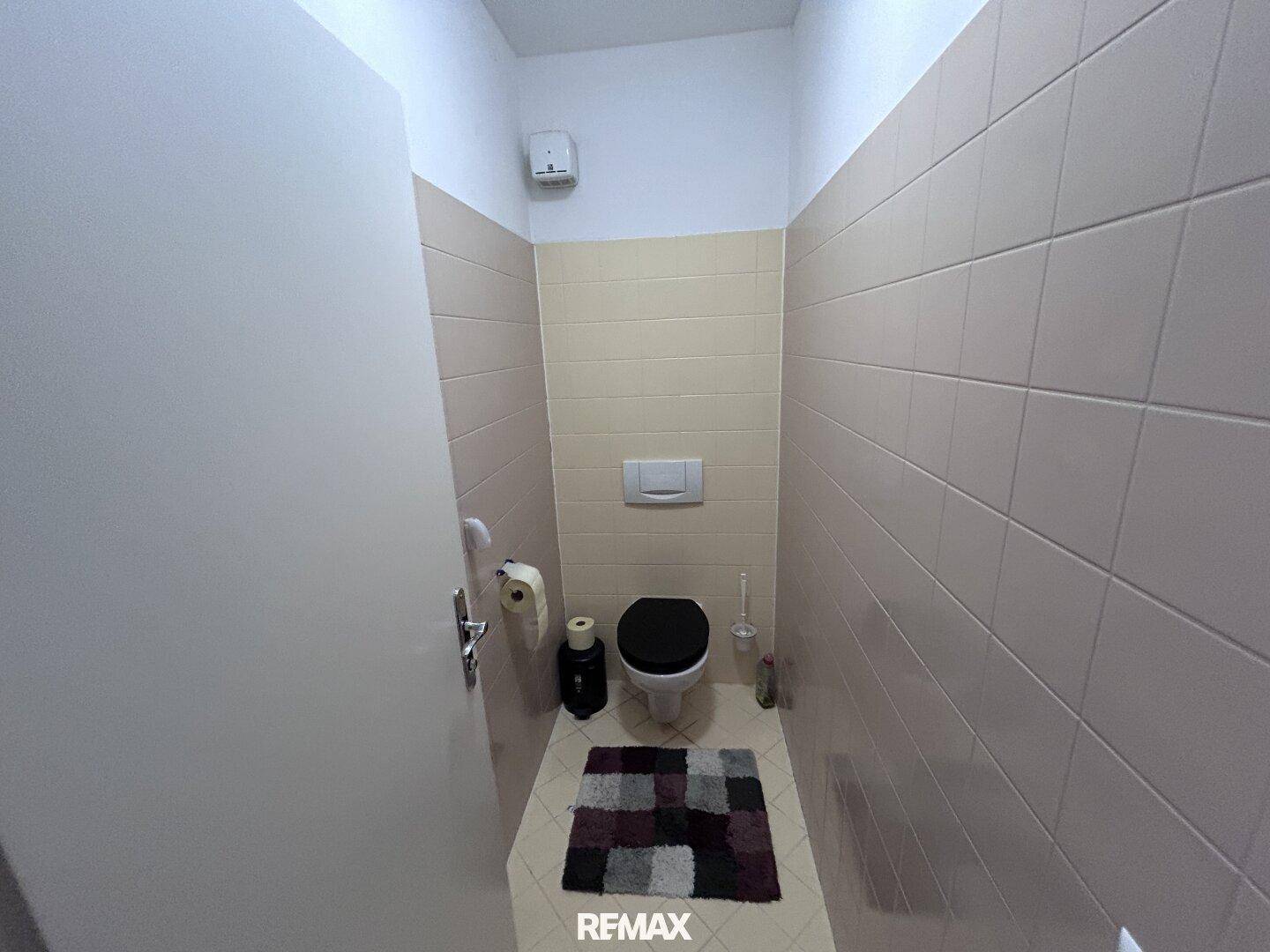 Kleines Gäste-WC mit Wand-WC und hellen Fliesen, funktional und sauber gestaltet.