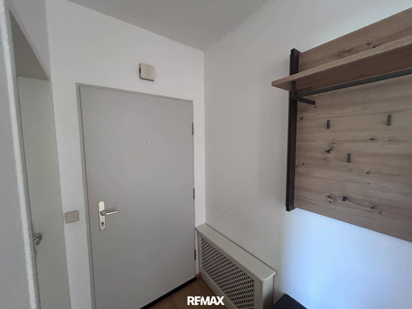 Eingangsbereich mit heller Tür, Heizkörper und einer praktischen Holzgarderobe an der Wand.
