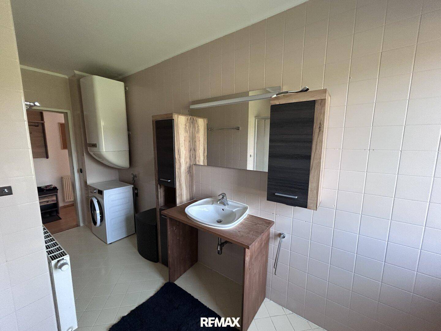 Badezimmer mit Waschtisch, Spiegelschrank und Waschmaschine, ausgestattet mit hellen Fliesen.