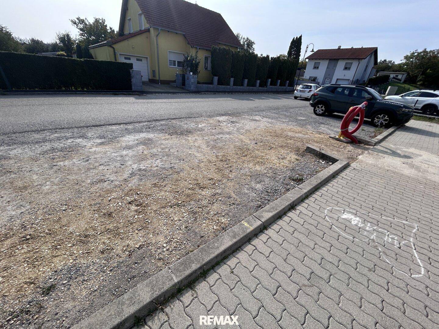 Außenbereich mit Schotterfläche und Fahrradständer, angrenzend an eine Wohnstraße mit Häusern.